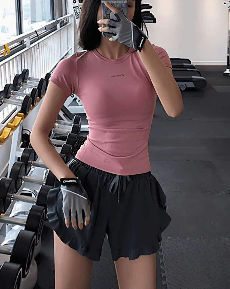 Woman wearing a pink breathable fitness t-shirt in a gym, showcasing running sportswear SF0039. Perfect for yoga, running, and gym workouts.